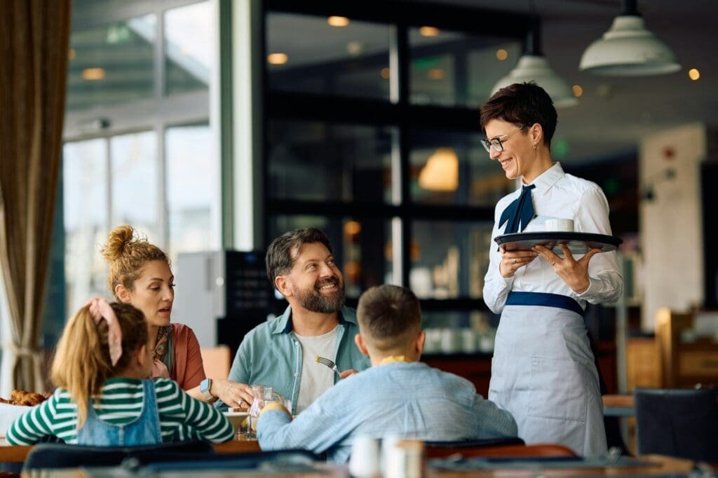 Happy hotel waitress serving family in a restaurant.