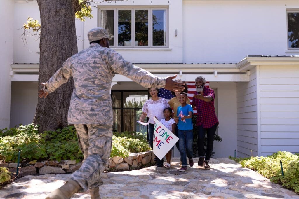 Multi-generation mixed race family welcoming an African American man wearing military uniform